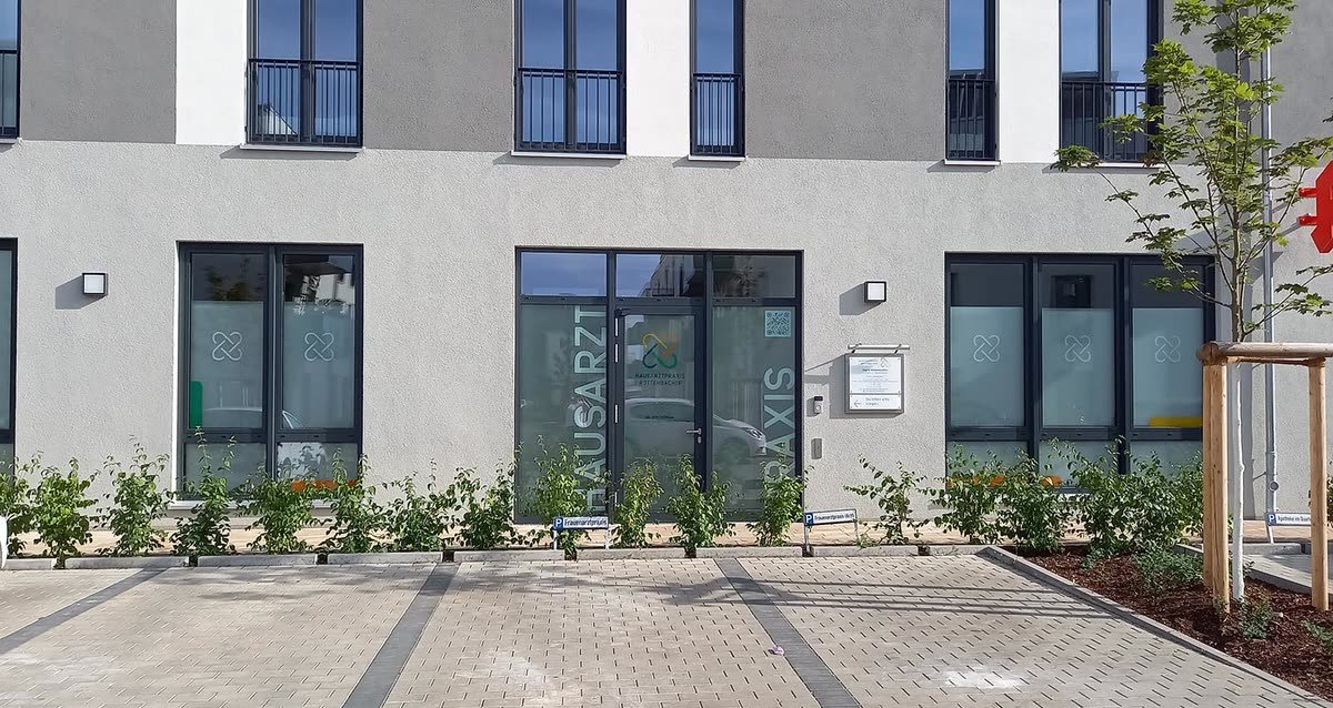 Haupteingang der Praxis auf der Innenhofseite, weiße Fassade mit Schriftzug Hausarztpraxis