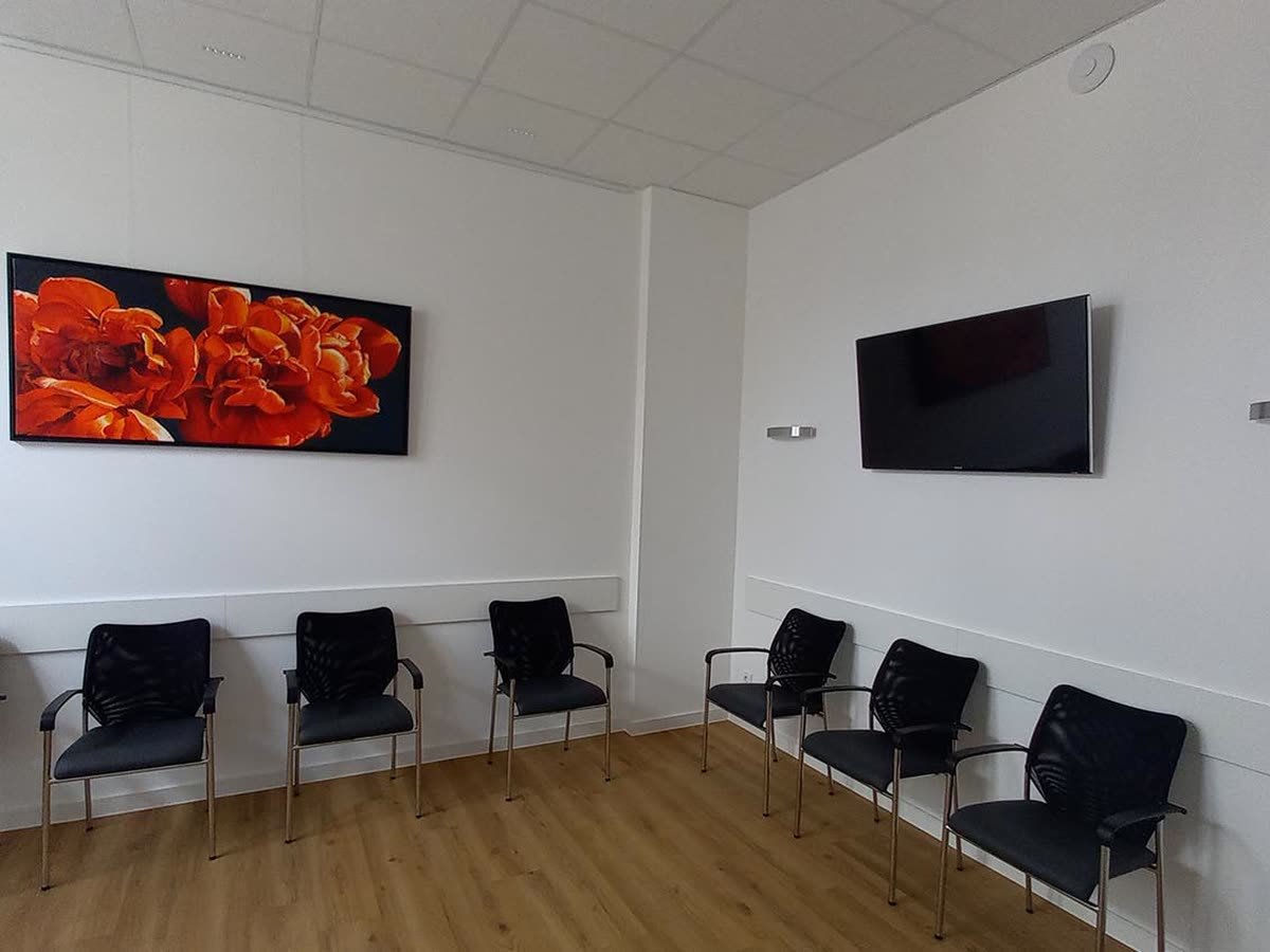 Wartezimmer mit Stuhlreihen, Wandbild und Fernseher